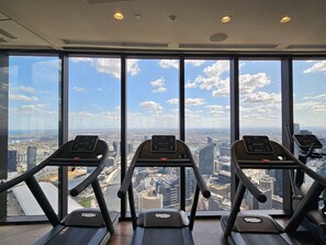 Drei Laufbänder in einem Fitnessstudio mit großen Fenstern und Blick auf die Stadt.