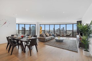 Ein modernes Wohnzimmer mit Essbereich, großen Fenstern und Blick auf die Stadt, einer Couch und einem Couchtisch.