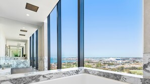 A modern bathroom with a large bathtub, a marble countertop, and a view of a cityscape through large windows.