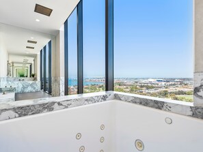 Ein modernes Badezimmer mit einer großzügigen Badewanne, einer Marmorarbeitsplatte und Blick auf Stadt und Wasser.