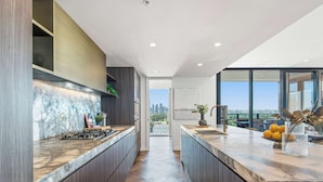 A modern kitchen with dark wood cabinets, a marble countertop, and a view of the city.