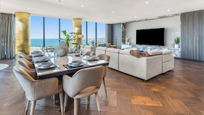 A modern living room with a large TV, a dining area with a table set for four, and a sofa set.