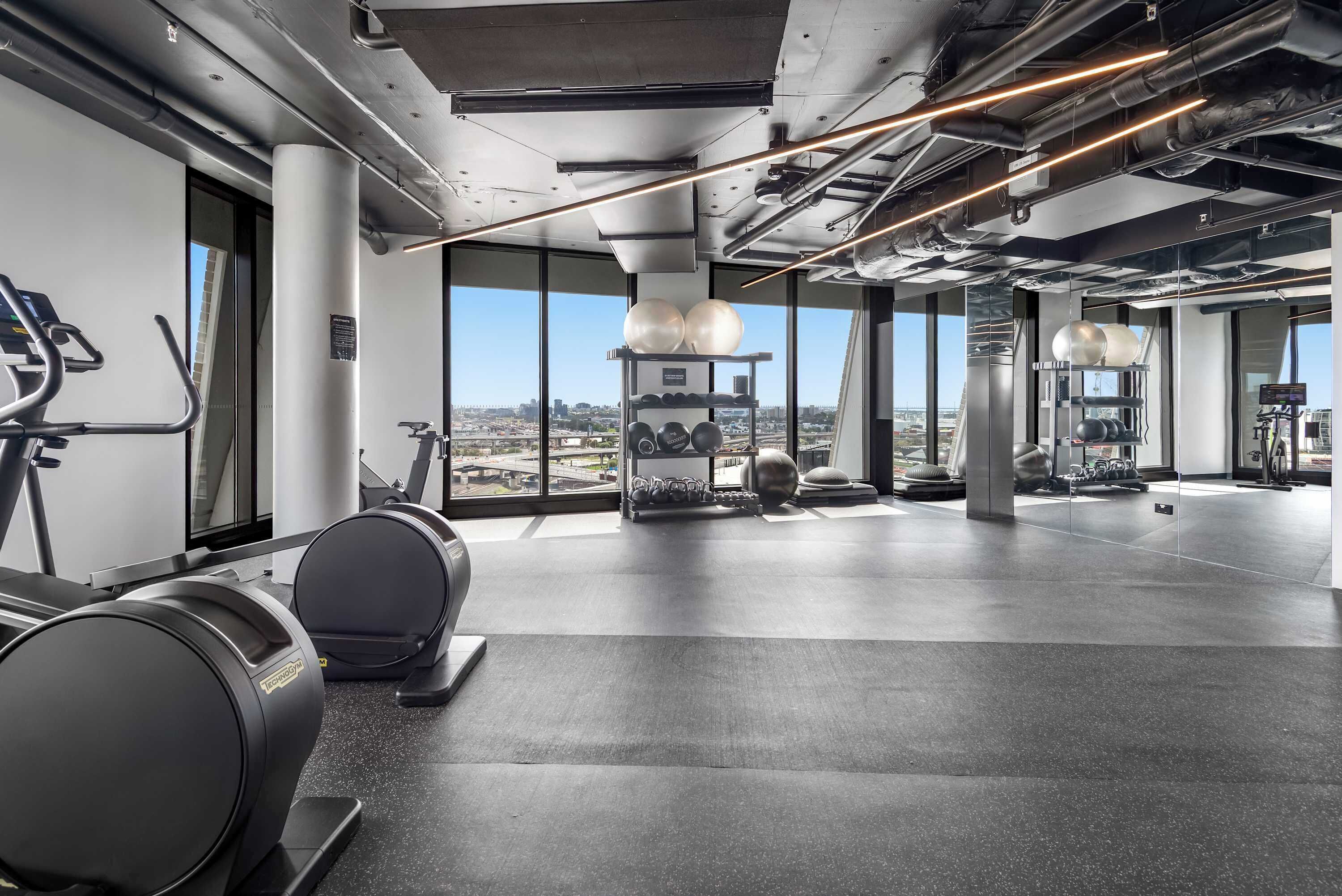A modern gym with exercise equipment, large windows, and a city view.
