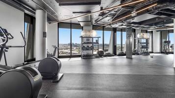 A modern gym with exercise equipment, large windows, and a city view.
