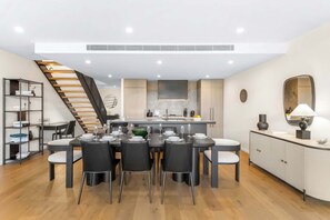 A modern kitchen with a central island, a dining area with a round table and chairs, a staircase, and a bookshelf. - Ultralux City Townhouse with Parking, Gym + Views (West Melbourne)
