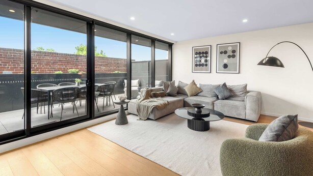 Ein modernes Wohnzimmer mit einem großen Schiebeglastür, die auf eine Terrasse im Freien führt, einem grauen Sofa, einem grünen Sessel und einem Couchtisch.