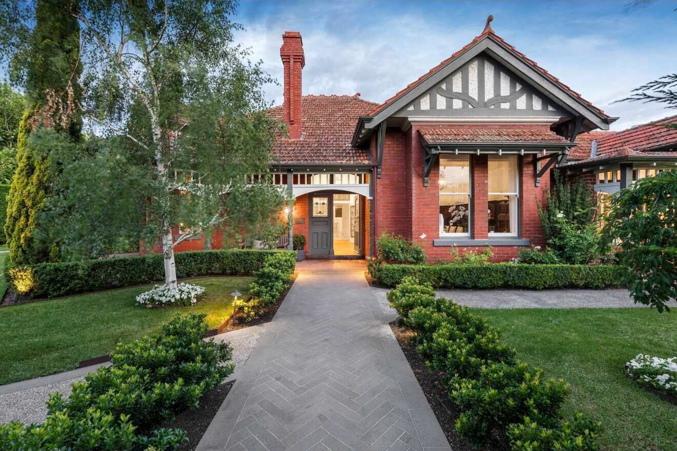 A brick house with a herringbone driveway, a chimney, and a well-maintained garden.