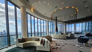 Uma sala de estar ampla com grandes janelas, um lustre moderno e um espaço de estar curvo.