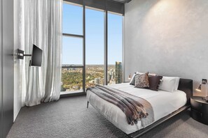 Ein modernes Schlafzimmer mit einem großen Bett, einem an der Wand montierten Fernseher und Stadtblick durch große Fenster.