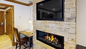 A stone fireplace with a TV above it, a dining table with chairs, and a wooden door in the background. - Ski-in/out gem with kitchenette, fast WiFi, onsite pool/hot tub, W/D, concierge (Vail)