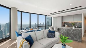 A modern living room with a sofa, dining area, and kitchen with a city view. - Live in the clouds! 3BD luxury apt. in Southbank. (Southbank)