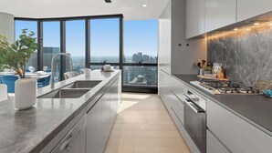 A modern kitchen with a large island, a stove, and a view of the city. - Live in the clouds! 3BD luxury apt. in Southbank. (Southbank)