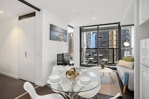 Un espace de vie moderne avec une table à manger en verre, des meubles blancs et une grande fenêtre donnant sur la ville.