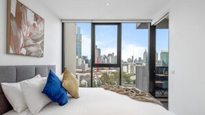 Un dormitorio moderno con una cama grande, vista a la ciudad y un cuadro en la pared.