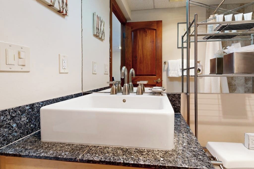 Une salle de bain avec un grand lavabo blanc, un comptoir en granit et une porte en bois.