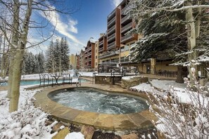Ett hotell med ett bubbelbad omgivet av snö, en pool och utsikt över ett berg.