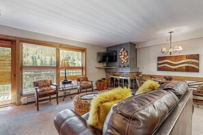 A living room with a leather sofa, wooden blinds, a fireplace, and a television. - Mountain view, ski-in/out condo w/ fireplace, fast WiFi, shared pool/hot tubs/WD (Vail)