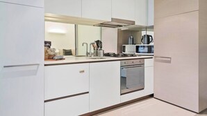 Une cuisine moderne avec des meubles blancs, une hotte en acier inoxydable, un four à micro-ondes et une bouilloire.
