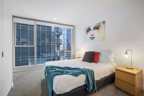 Ein Schlafzimmer mit großem Fenster, einem Bett, einem Nachttisch und einem an der Wand hängenden Bild.