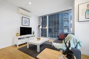 Ein modernes Wohnzimmer mit Flachbildfernseher, weißen Möbeln, einem großen Fenster und einem dekorativen Geweih.