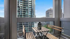 Een balkon met een houten tafel en stoelen, een lantaarn en uitzicht op hoge gebouwen.