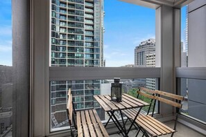 Ein Balkon mit Holztisch und Stühlen, einer Laterne und Blick auf hohe Gebäude.