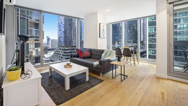 Een moderne woonkamer met een bank, salontafel en stoelen, grote ramen met uitzicht over de stad en een wit plafond.