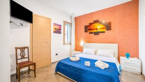 Une chambre d’hôtel avec un lit, une chaise, une télévision, une fenêtre et des œuvres d’art accrochées au mur.