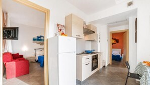 Une cuisine compacte équipée d’un réfrigérateur, d’une cuisinière et d’un four. Un coin repas est aménagé avec une table et des chaises.