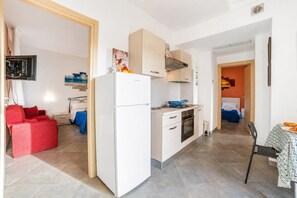 A compact kitchen with a refrigerator, stove, and oven. There is a dining area with a table and chairs. - Pino 2 -3 Bedrooms Near The Sea, Nardò, Italy (Nardò)