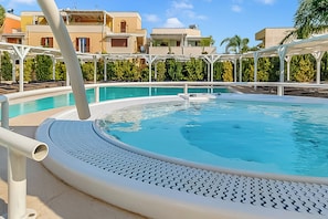 Ein Swimmingpool mit weißer Liegefläche, umgeben von Gebäuden mit Balkonen und wolkenlosem Himmel.