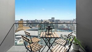 Un balcón con vistas a la ciudad, una mesa con sillas y una planta en maceta.