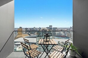 Ein Balkon mit Blick auf eine Stadtlandschaft, einem Tisch mit Stühlen und einem Blumentopf.