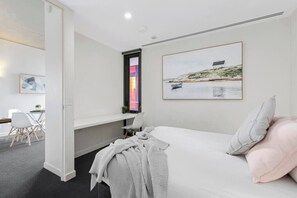 Ein Schlafzimmer mit einem Bett, einem Schreibtisch und einem Stuhl. Ein Fenster bietet einen Blick auf eine Landschaft.