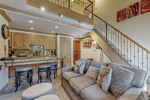 A spacious living area with a high ceiling, a staircase, and a kitchen with wooden cabinets. - Mountain view, ski-in/out condo w/ fireplace, fast WiFi, shared pool/hot tub/WD (Vail)