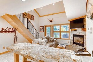 A living room with a fireplace, a sofa, a coffee table, and a staircase. - Mountain view, ski-in/out condo w/ fireplace, fast WiFi, shared pool/hot tub/WD (Vail)