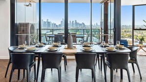 Zona pranzo con vista sullo skyline cittadino, ampie finestre e arredamento moderno.