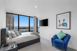 A modern bedroom with a large bed, a blue armchair, a mounted TV, and a city view. - Oasis above the clouds in ultra-lux city penthouse (Southbank)