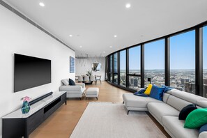A modern living room with a large TV, a sofa, and a dining area with a view of the city. - Oasis above the clouds in ultra-lux city penthouse (Southbank)
