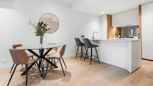 Eine moderne Küche mit einer zentralen Kochinsel, einem Essbereich mit rundem Tisch und Stühlen sowie einem großen Spiegel an der Wand.