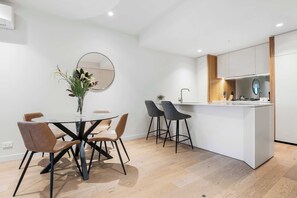 Eine moderne Küche mit einer zentralen Kochinsel, einem Essbereich mit rundem Tisch und Stühlen sowie einem großen Spiegel an der Wand.