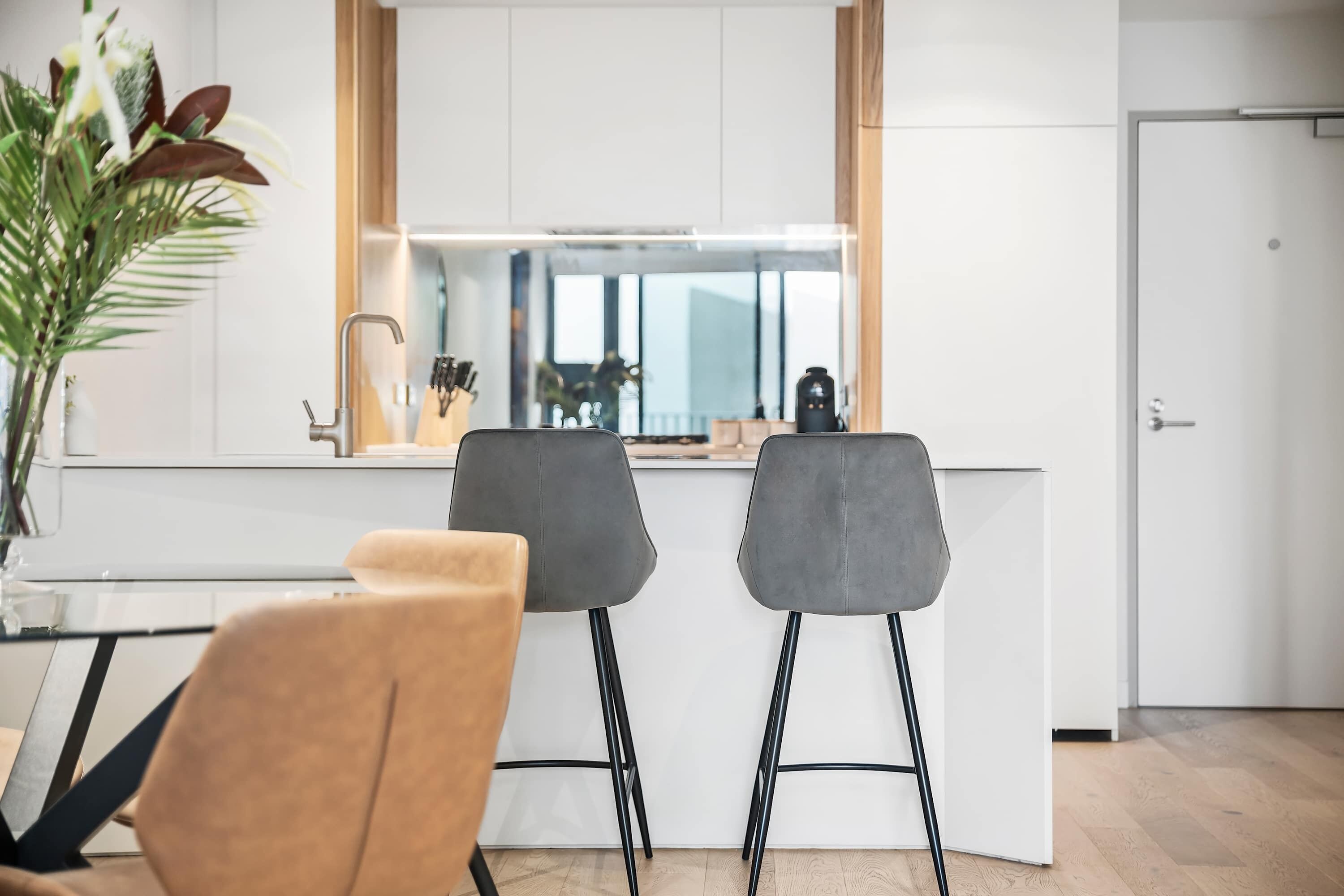 Cocina moderna con dos taburetes de bar, una encimera blanca y una puerta.