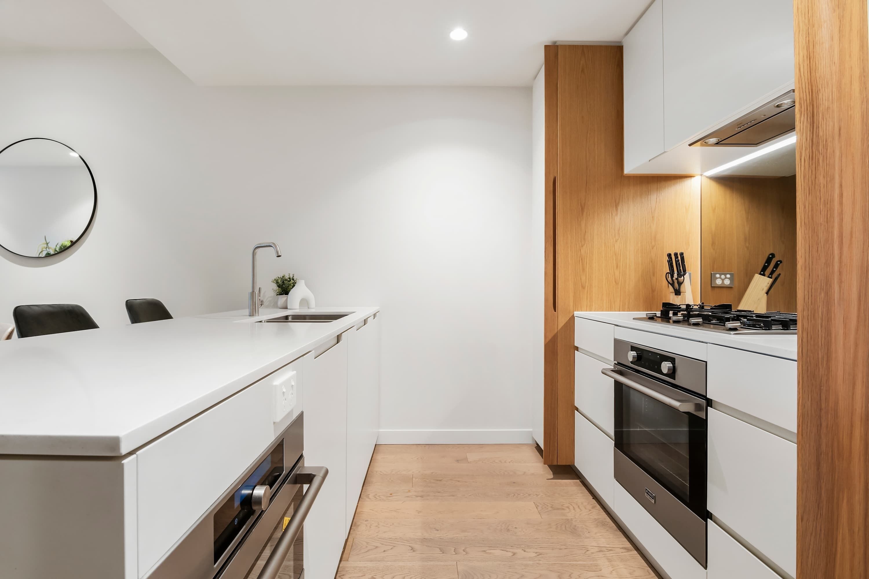Eine moderne Küche mit weißen Schränken, einer zentralen Kochinsel, Edelstahlgeräten und einer Akzentwand aus Holz.