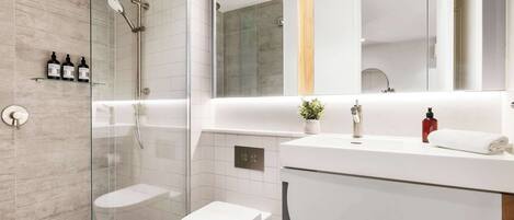 Une salle de bain moderne avec une douche à parois de verre, des toilettes, un lavabo avec un miroir et une petite plante posée sur le comptoir.