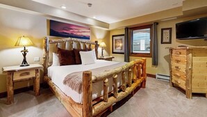A bedroom with a wooden bed, bedside tables, a dresser, a television, and a painting on the wall. - Ski-in/ski-out Lionshead Village condo with hot tubs, pool, gym - steps to lifts (Vail)