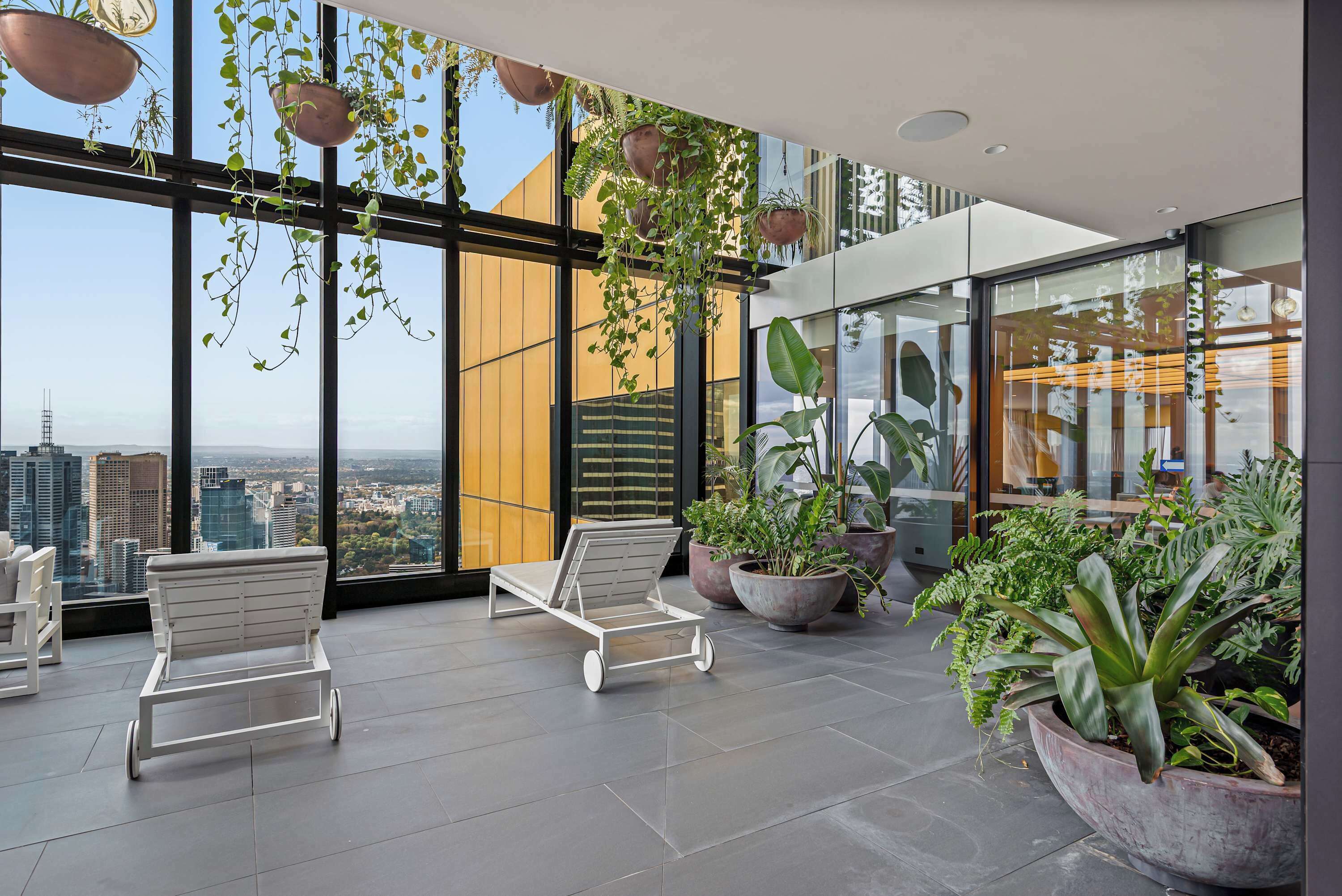 Un espace de détente moderne, doté de grandes fenêtres, de plantes en pot et de fauteuils blancs.