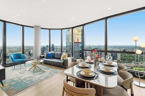 A modern dining area with a city view, a sofa, a blue chair, and a table set for dining. - Live in the clouds! 3BD luxury apt. in Southbank (Southbank)