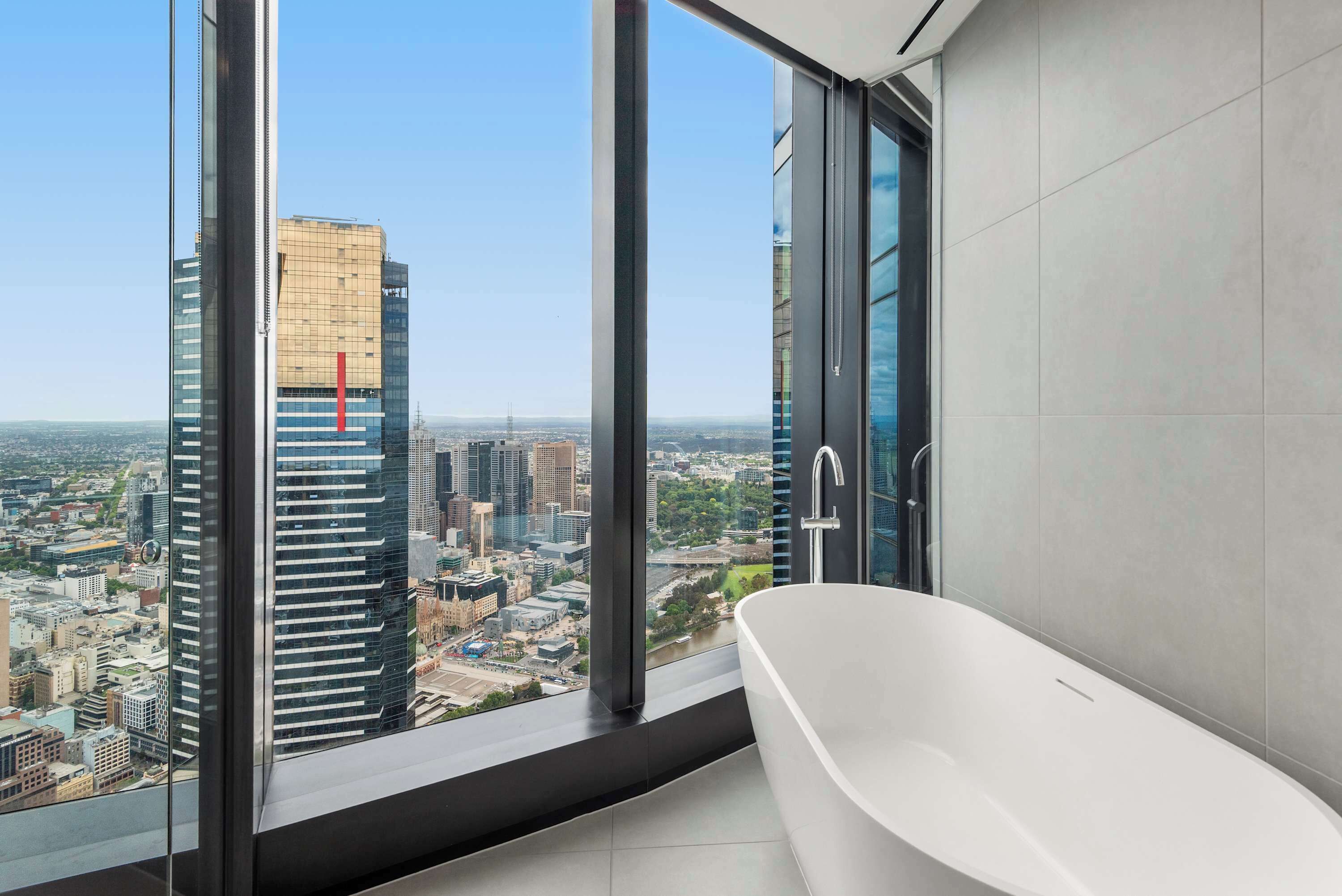 A modern bathroom with a large bathtub, a view of a cityscape through floor-to-ceiling windows, and a sleek, contemporary design.