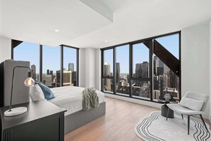 Ein modernes Schlafzimmer mit Blick auf die Stadt, inklusive Bett, Schreibtisch und Sessel.
