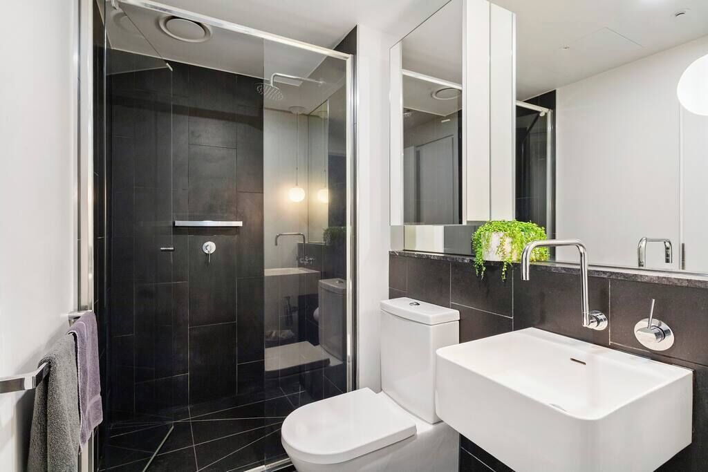 A modern bathroom with a glass-enclosed shower, a white toilet, and a large sink with a mirror above.